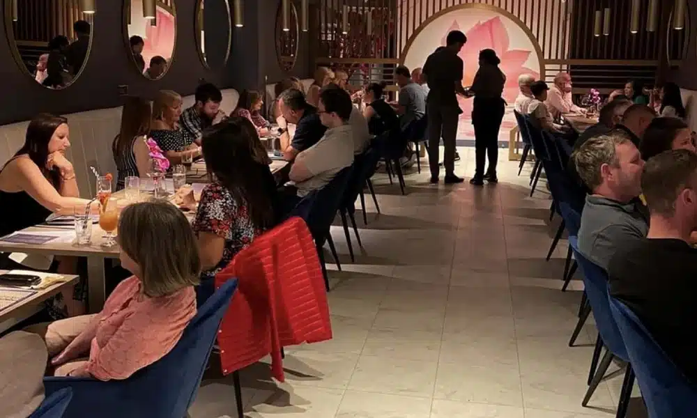 Guests dining at Korat Thai restaurant, seated on blue velvet chairs and booth seating in a lively evening service.
