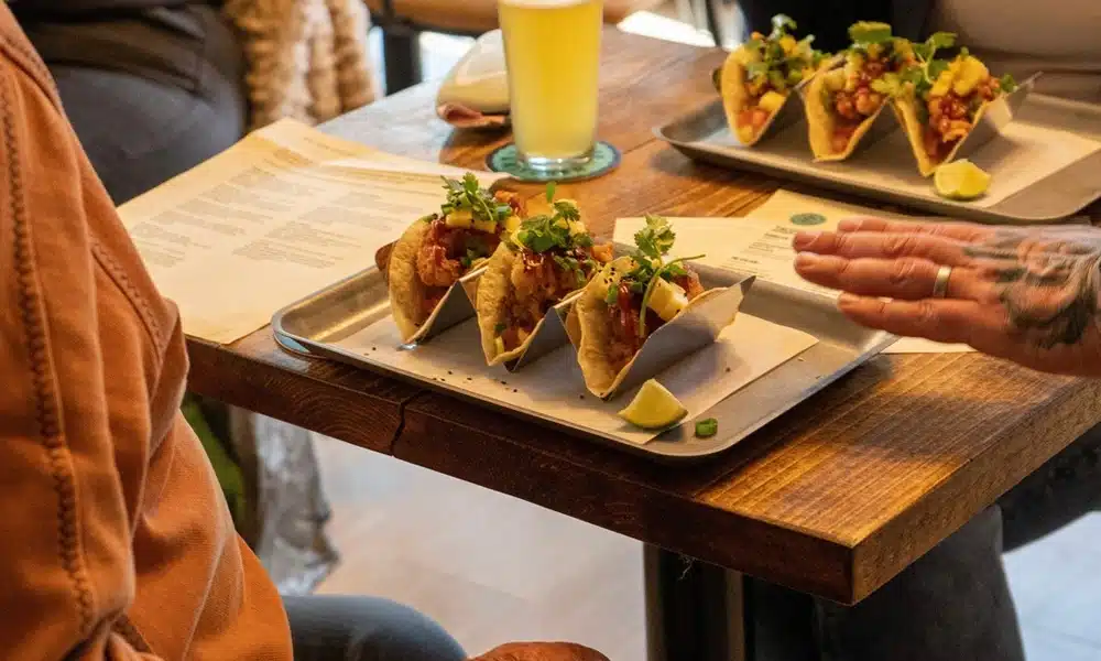 Close-up of a solid oak table top at Legra Tap & Kitchen with tacos and drinks showcasing the natural wood grain.