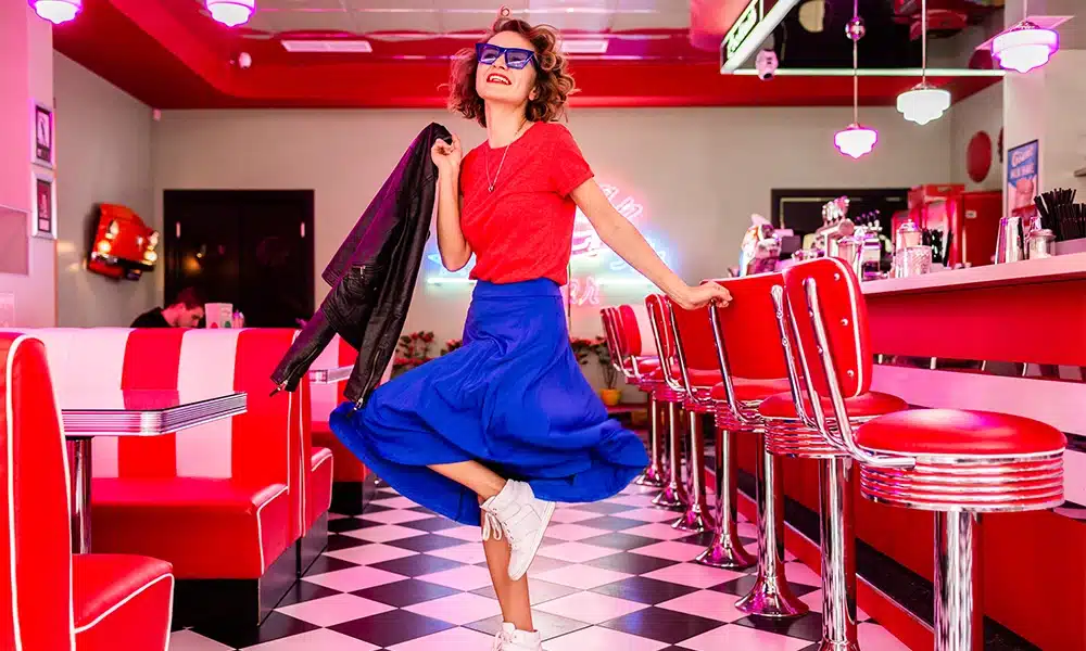 Woman standing posing in an American diner surrounded by retro booth seating, chrome chairs and vintage décor
