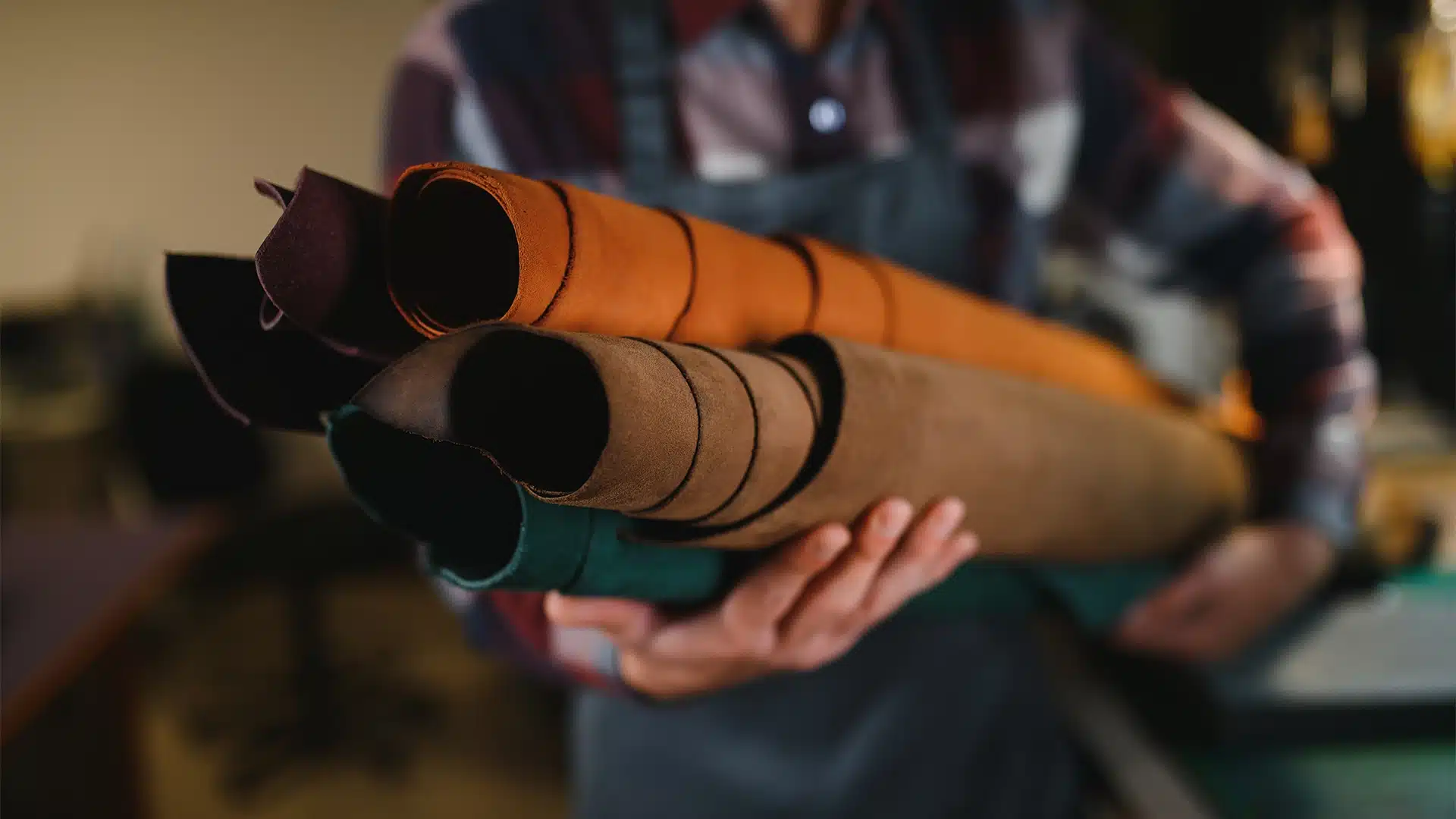 Man holding four rolls of leather looking fabric in a workshop